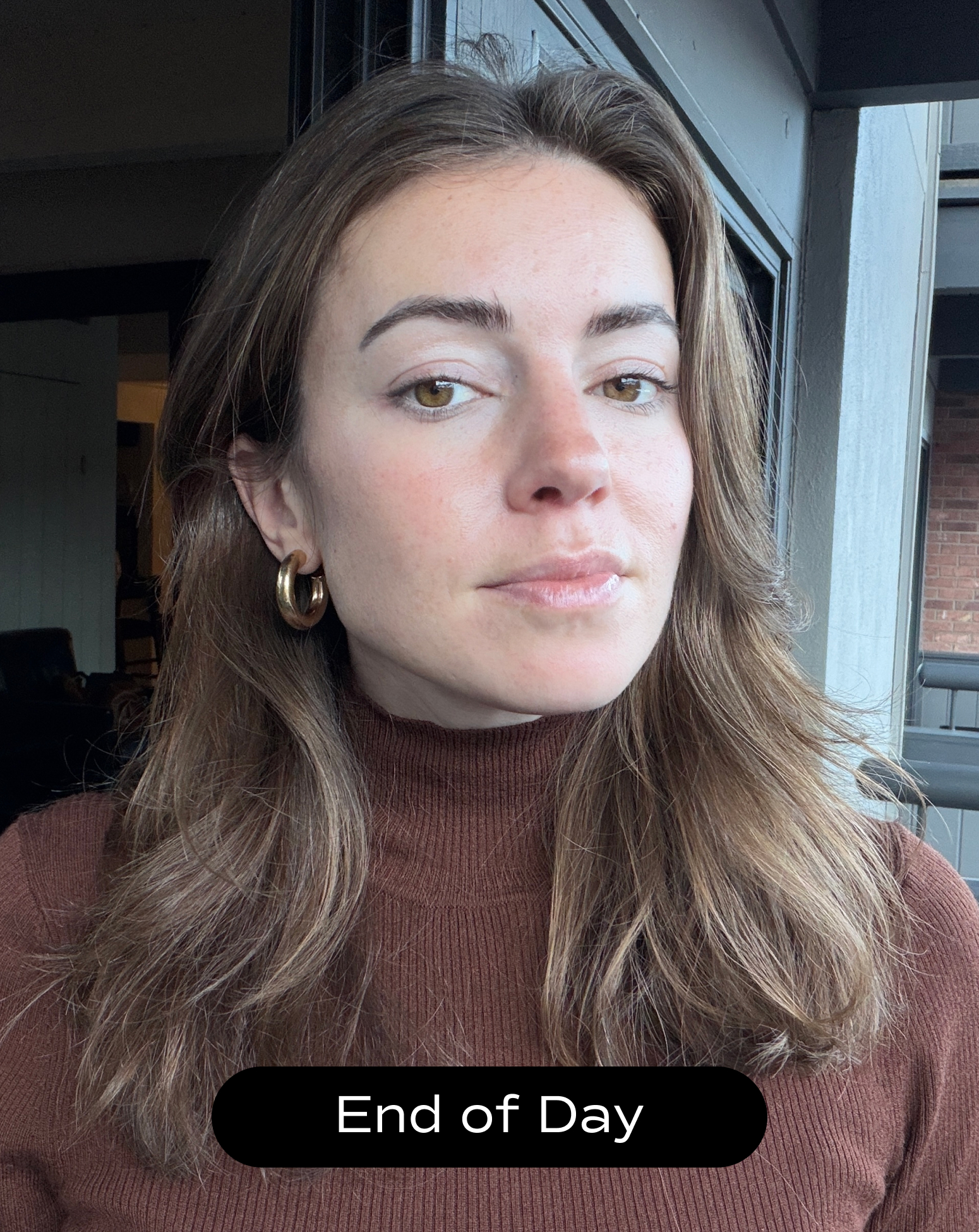 A woman with long brown hair wearing a brown turtleneck and gold hoop earrings stands indoors with a neutral expression. The caption at the bottom reads "End of Day.
