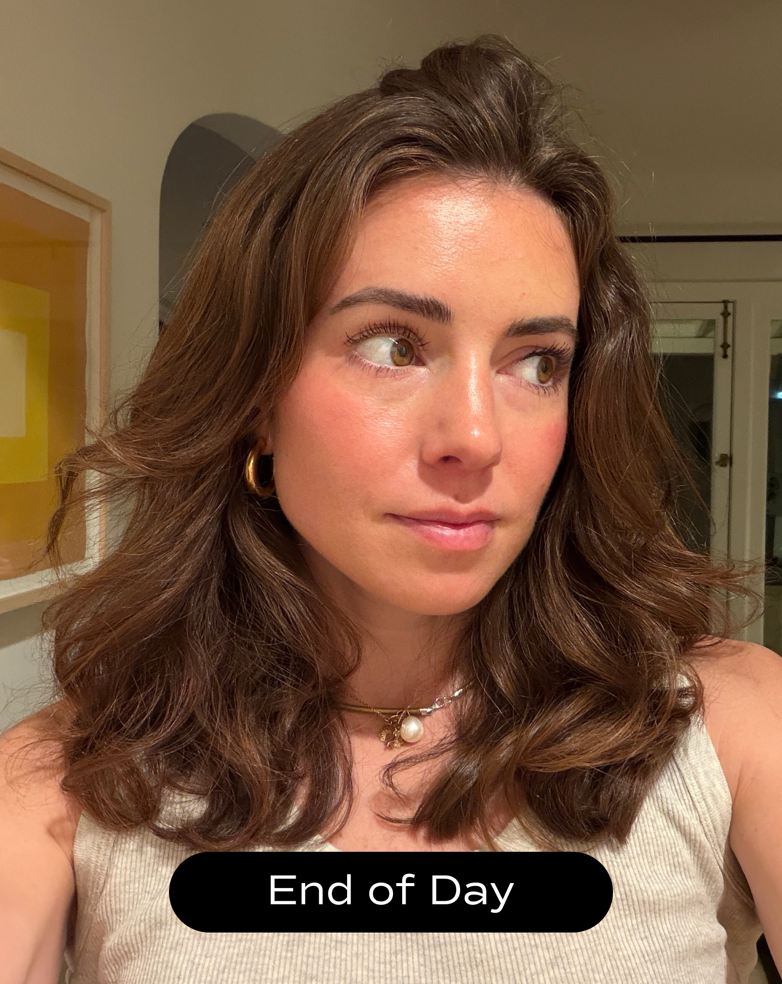 A woman with wavy brown hair and gold hoop earrings looks to the side indoors. She wears a beige tank top and layered necklaces. A label at the bottom reads "End of Day.