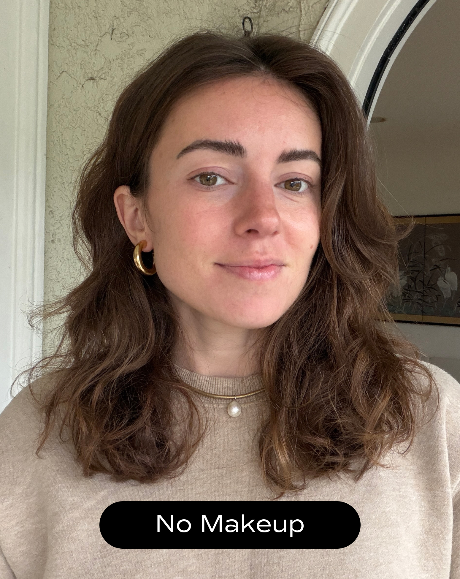 A woman with shoulder-length brown hair and gold hoop earrings looks at the camera, wearing a beige sweater. Text at the bottom reads “No Makeup.”.