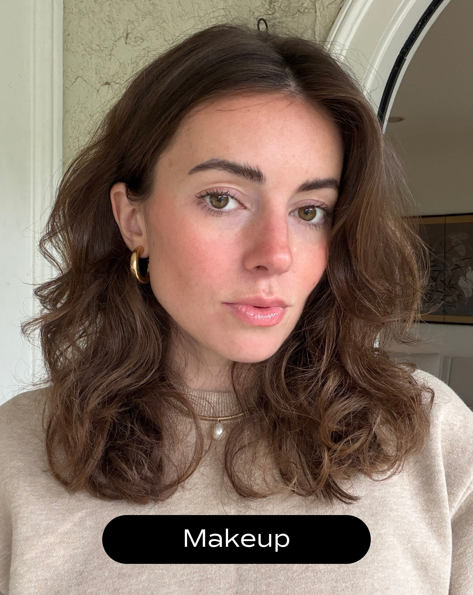 A woman with wavy brown hair and light makeup looks at the camera, wearing a beige top and gold hoop earrings. The word "Makeup" appears in a black oval at the bottom.