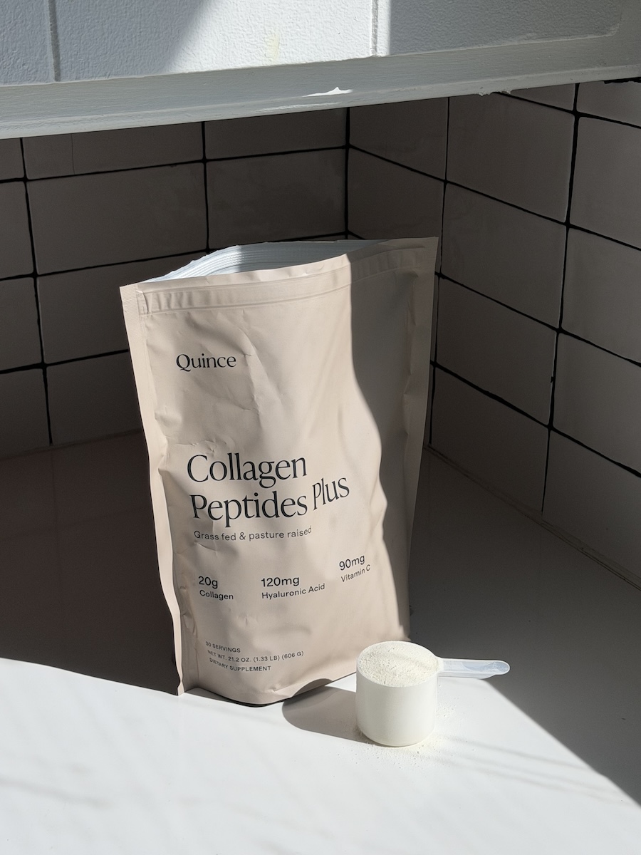 A beige pouch labeled "Quince Collagen Peptides Plus" stands on a white surface next to a plastic scoop filled with white powder.