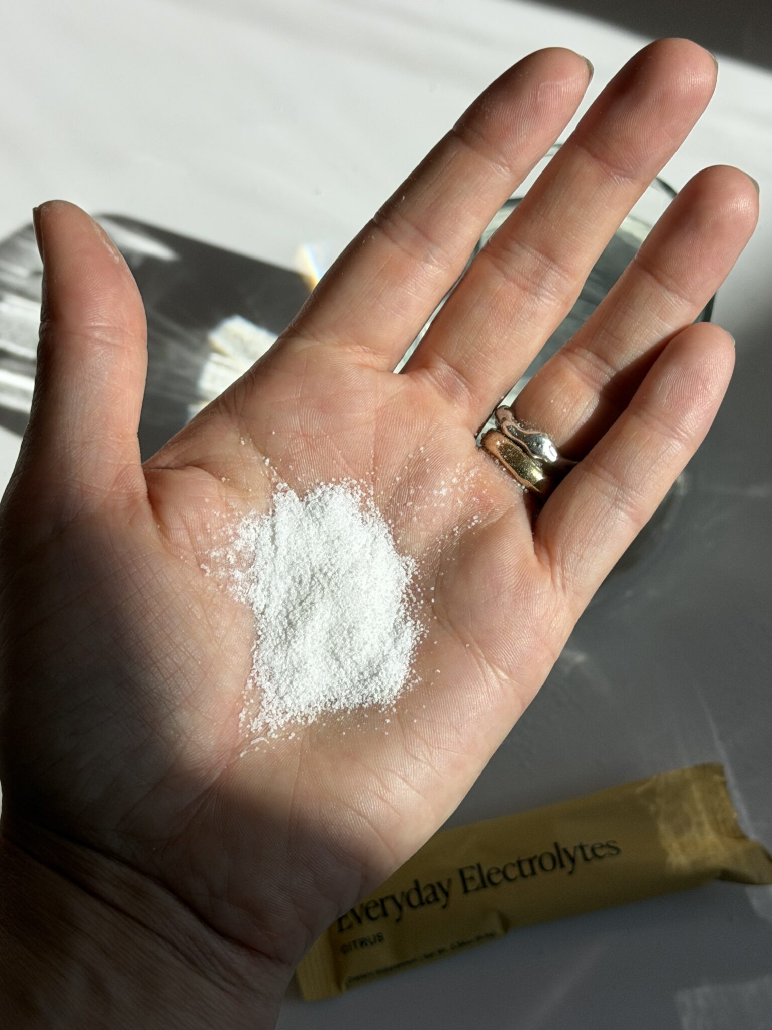 A hand holding a small mound of white powder, with a yellow packet labeled "everyday electrolytes" partially visible in the background.