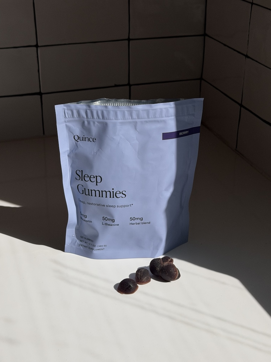 A bag of Quince Sleep Gummies labeled "Berry" stands on a white surface, with several gummies placed in front of the bag.