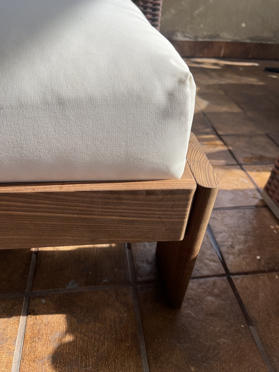 Close-up of a white cushion on a wooden chair or bench, shown on a sunlit tiled floor.