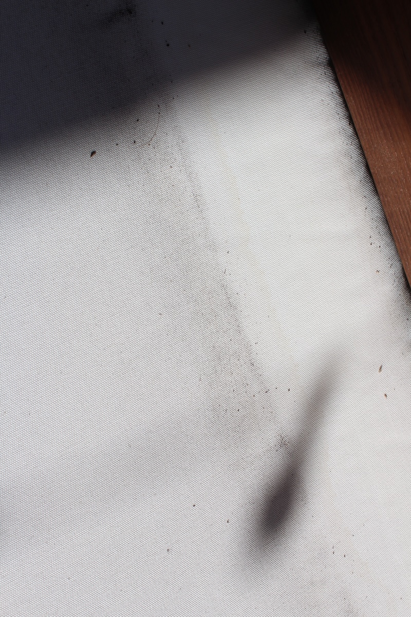 A white surface with a smudge of black dirt or dust, a shadow, and part of a wooden object visible in the corner.