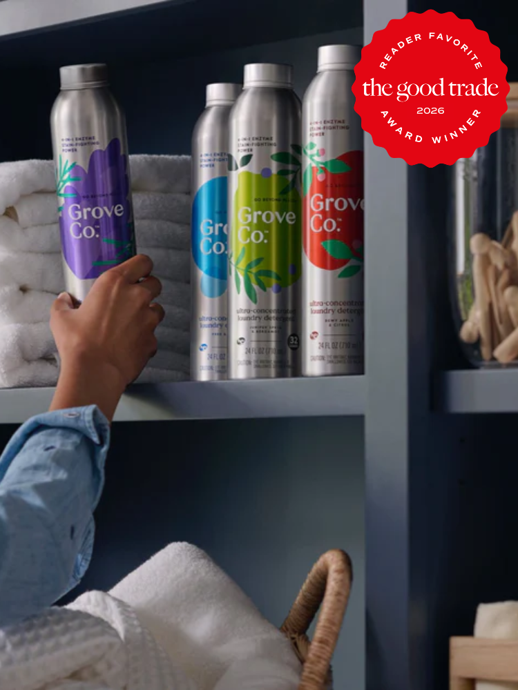A person places a bottle of Grove Co. cleaning product on a shelf alongside other bottles, folded towels, and a basket, with a "The Good Trade 2026 Award Winner" badge in the corner.