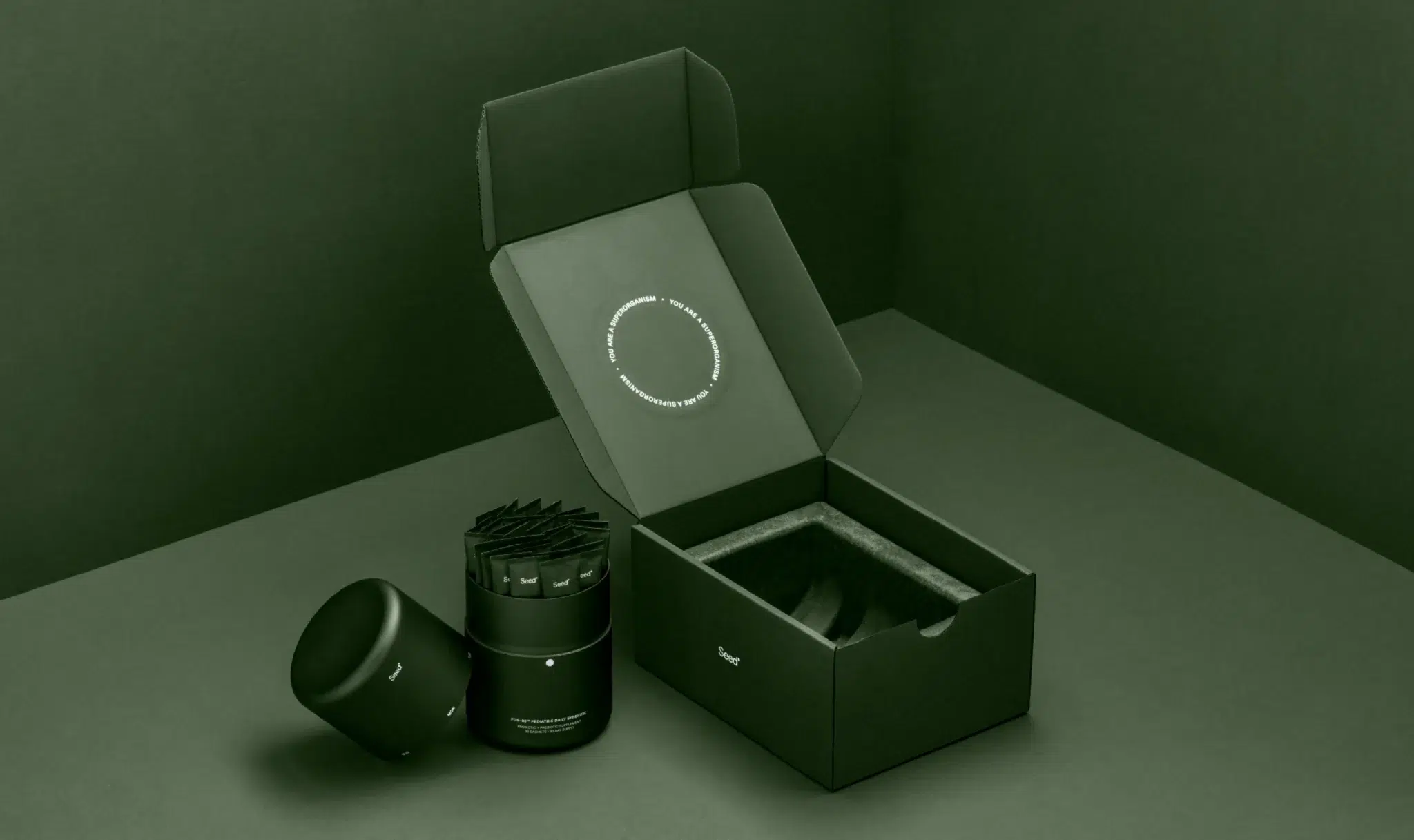 A matte black product container, lid, and a cylindrical item are displayed next to an open, foam-padded black box with a circular design printed inside the lid.