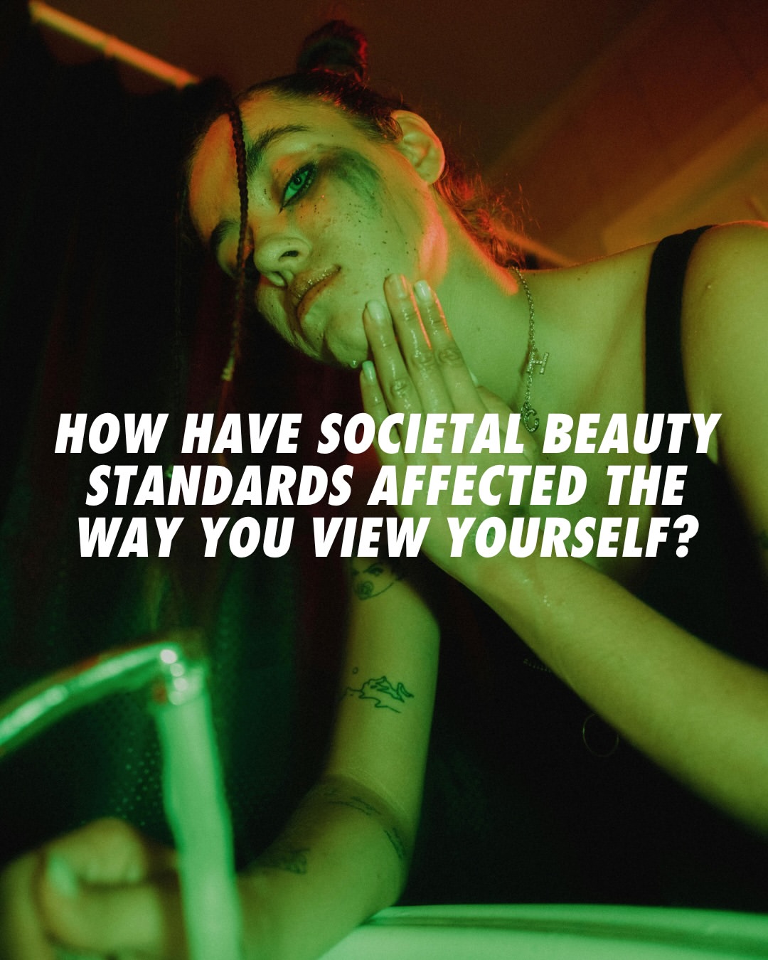 Person with smeared makeup looking into a mirror in dim light; bold text over image reads, “How have societal beauty standards affected the way you view yourself?”.