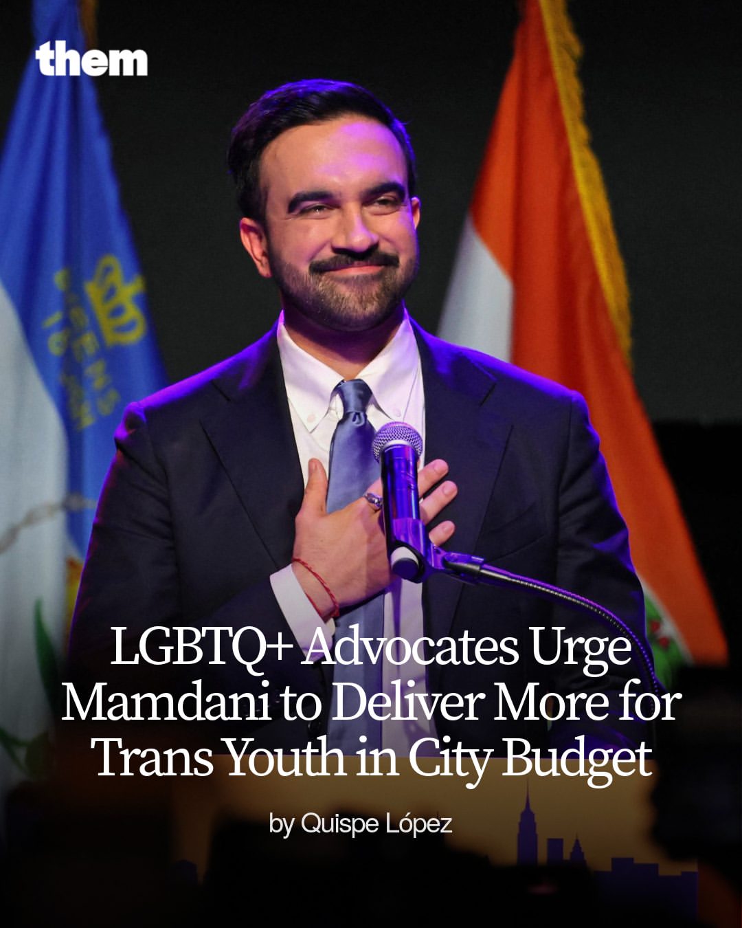 A man in a suit stands at a podium with one hand over his chest, smiling, in front of flags, with text urging more city budget support for trans youth.
