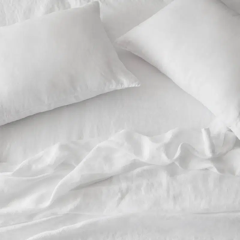 Two white pillows and a white sheet lie on a neatly made bed with slight wrinkles visible on the fabric.