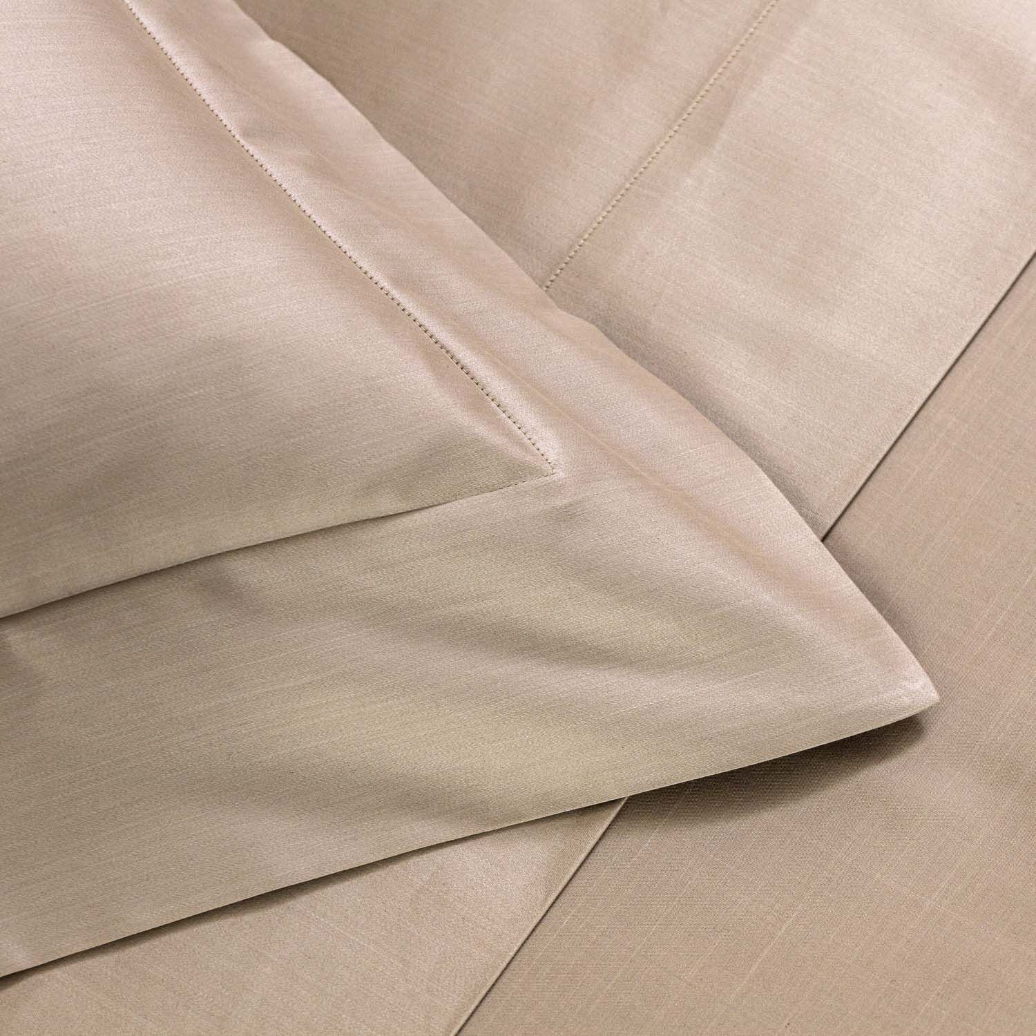 Close-up view of beige bed sheets and pillowcases neatly arranged on a bed, showing the fabric texture and stitching details.