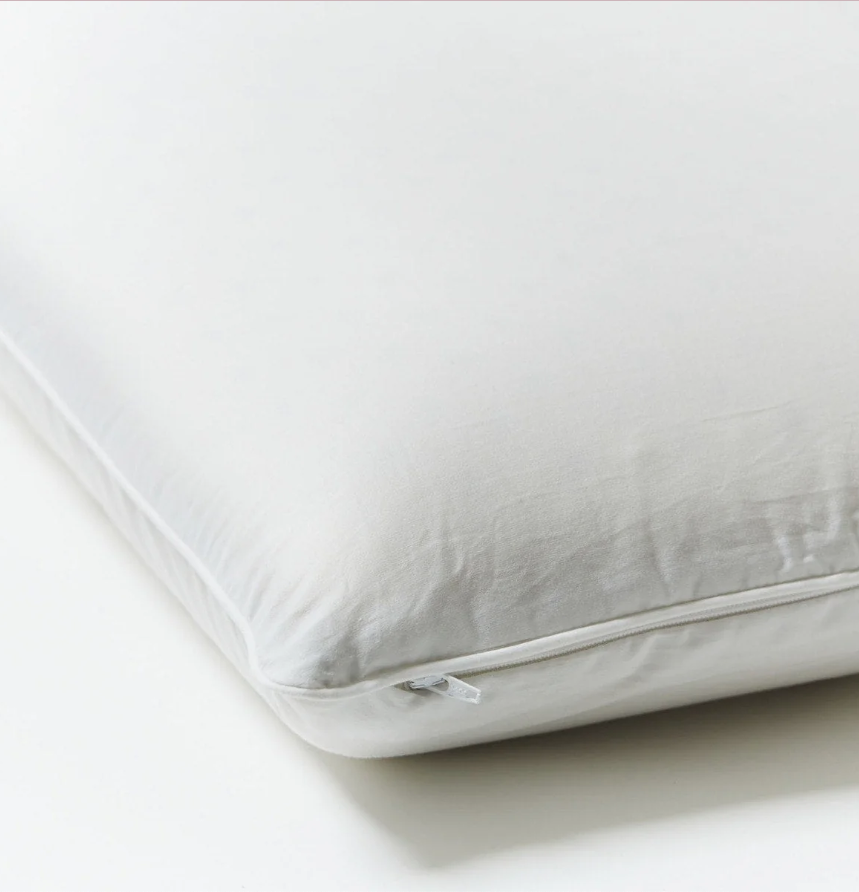 A close-up view of a white pillow with a visible zipper on one side, placed on a white surface.
