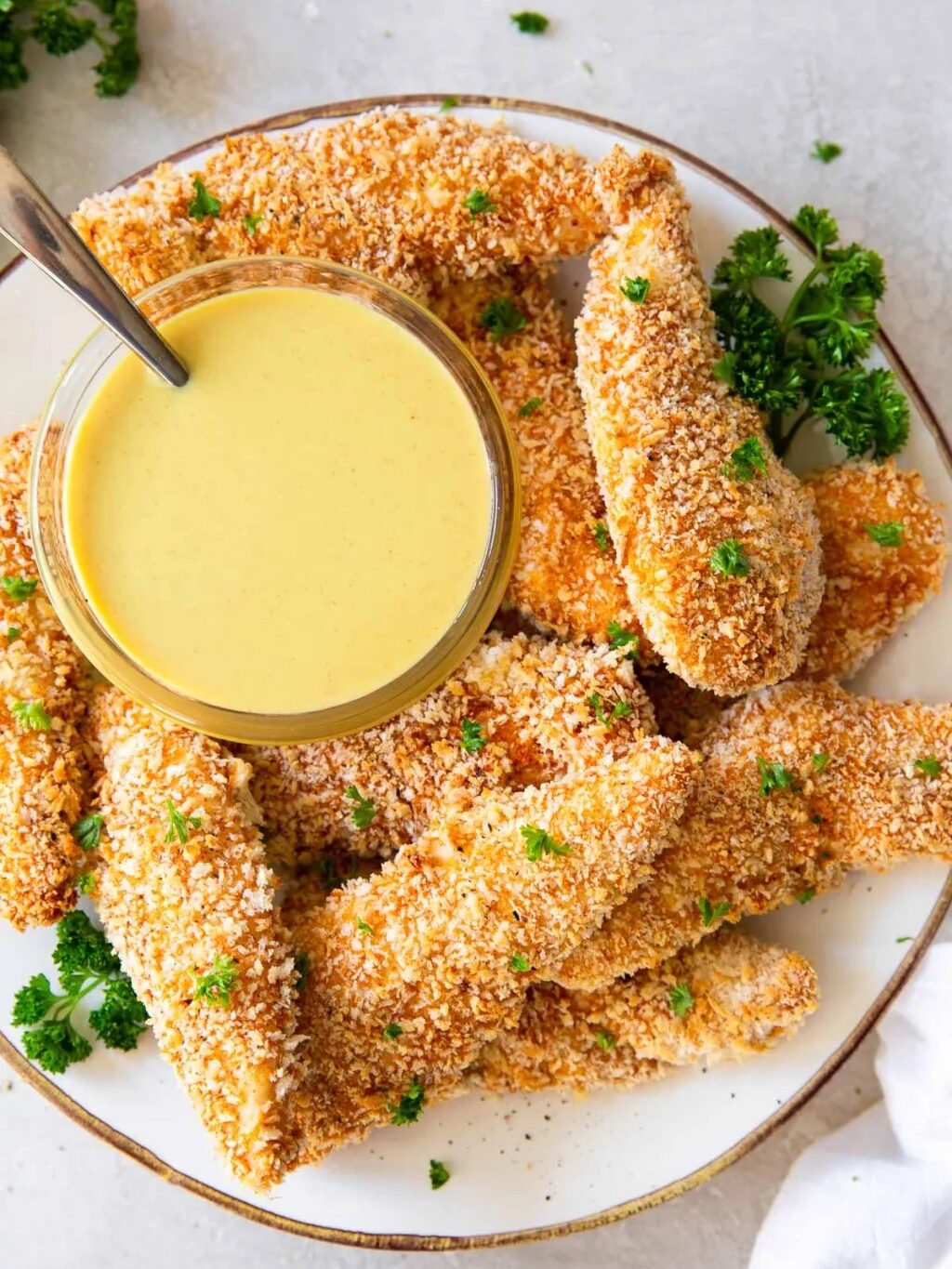 A plate of breaded chicken tenders garnished with parsley, served with a bowl of yellow dipping sauce.