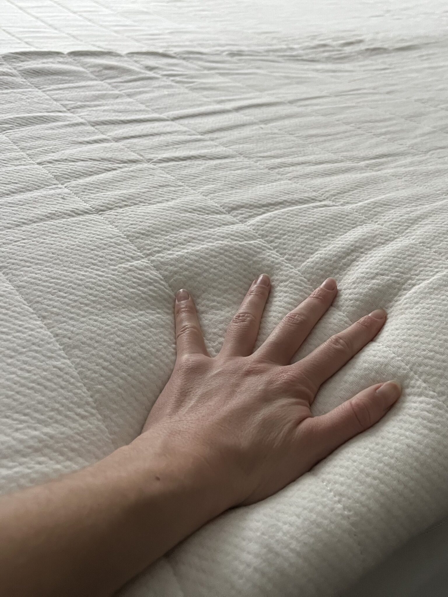 A hand pressing down on a white, textured mattress topper placed on a bed.