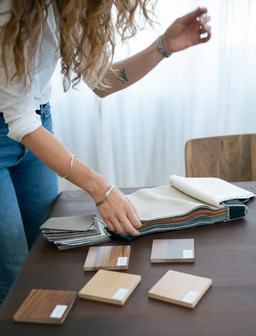 A person examines fabric swatches and wood samples on a table, possibly for interior design or decor selection.