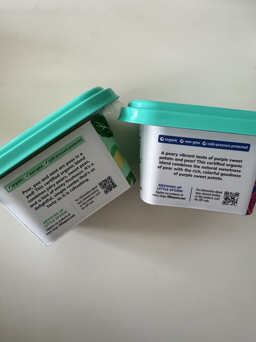 Two rectangular food containers with teal lids are shown. The labels indicate they contain an organic, non-GMO blend of pear and purple sweet potato. QR codes are visible on each label.