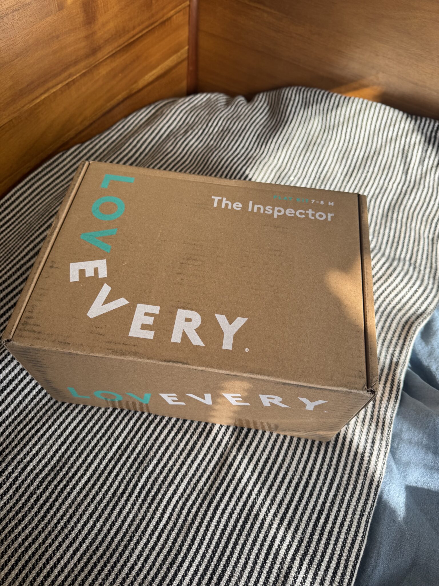 A Lovevery subscription box labeled "The Inspector" sits on a striped bedspread in sunlight.