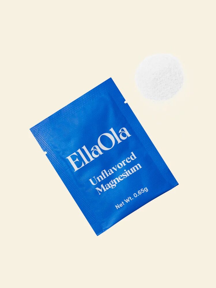 A blue packet labeled "EllaOla Unflavored Magnesium" lies next to a small mound of white magnesium powder on a light background.