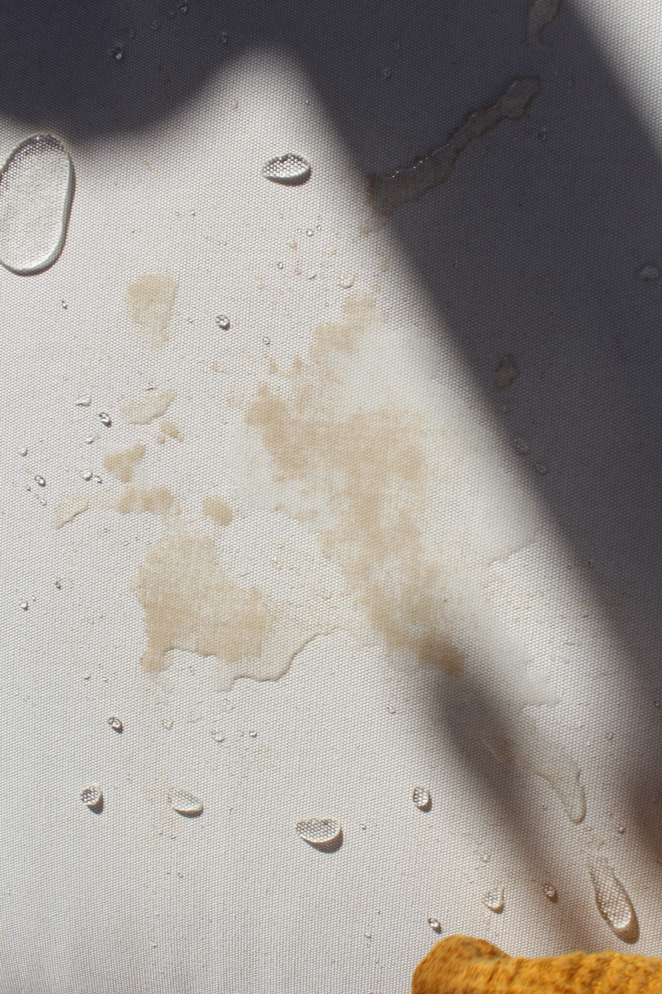 Spilled liquid and water droplets on a white surface with a shadow and a yellowish object partially visible in the corner.