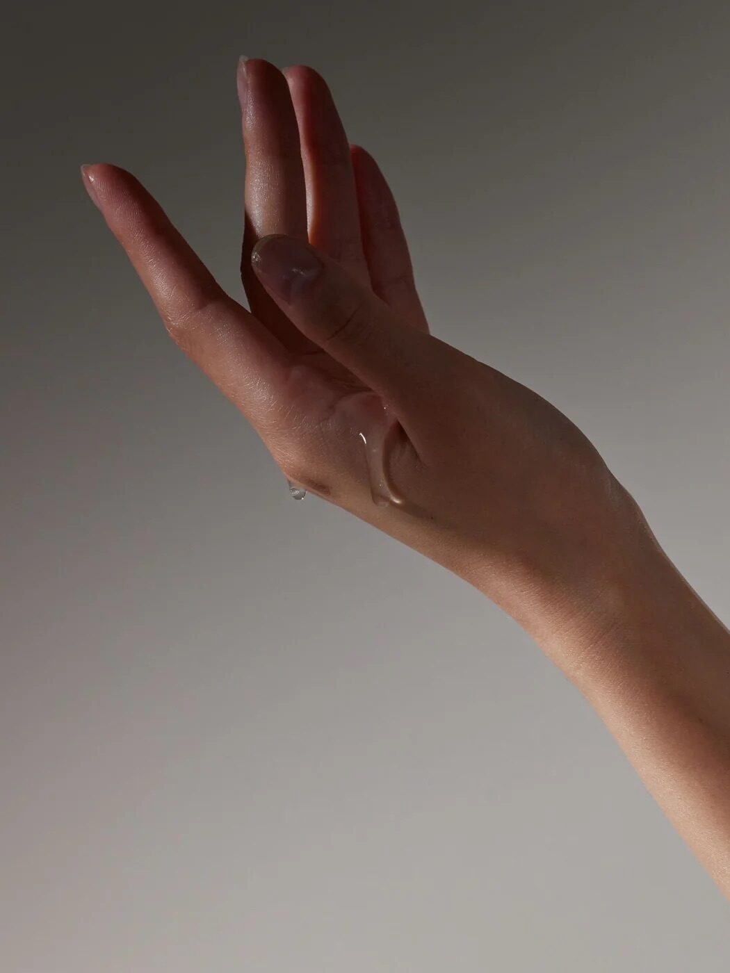 A close-up of a hand and forearm raised against a plain grey background with a small amount of clear liquid on the skin.