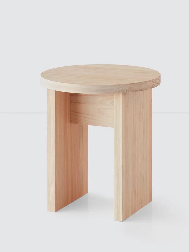 A small, light wood stool with a round top and three rectangular legs, placed against a plain white background.