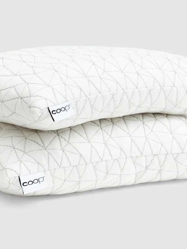 Two white quilted pillows with a geometric pattern and "coop" tags stacked on top of each other against a plain light background.