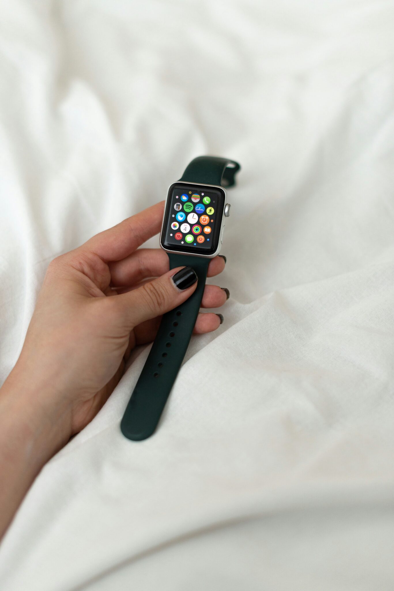 A person holding a black smartwatch with colorful app icons displayed on the screen, against a white fabric background.
