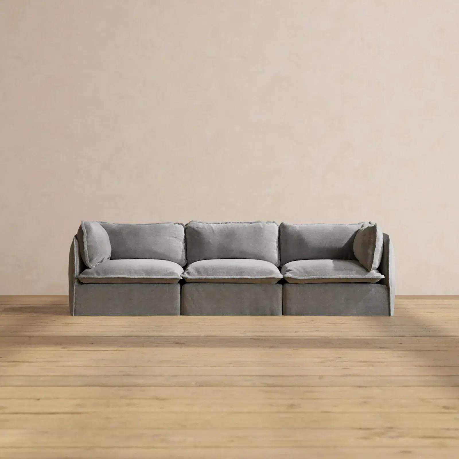 A gray three-seater sofa with plush cushions sits on a light wood floor against a plain beige wall.