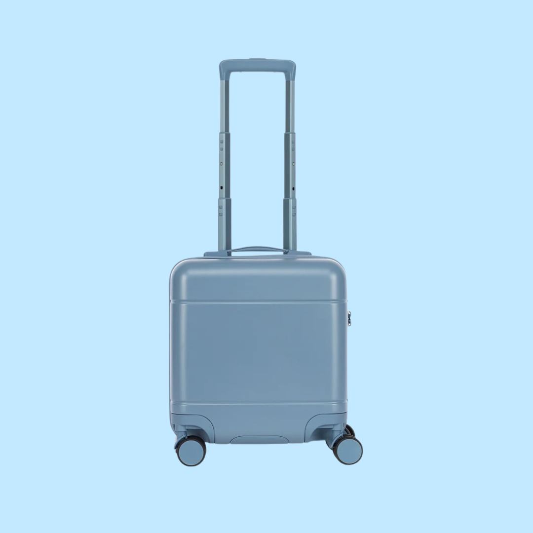 A small, hard-shell, blue suitcase with four wheels and a telescoping handle, shown against a light blue background.