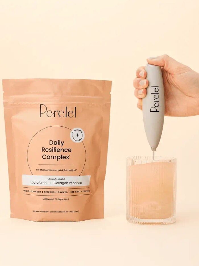 A hand uses a frother to mix a drink in a glass beside a stand and a Perlelel Daily Resilience Complex supplement pouch on a beige surface.