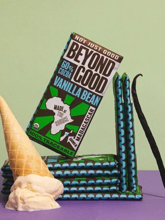 A stack of Beyond Good vanilla bean chocolate bars is displayed with a melting ice cream cone and a vanilla bean pod against a pastel background.