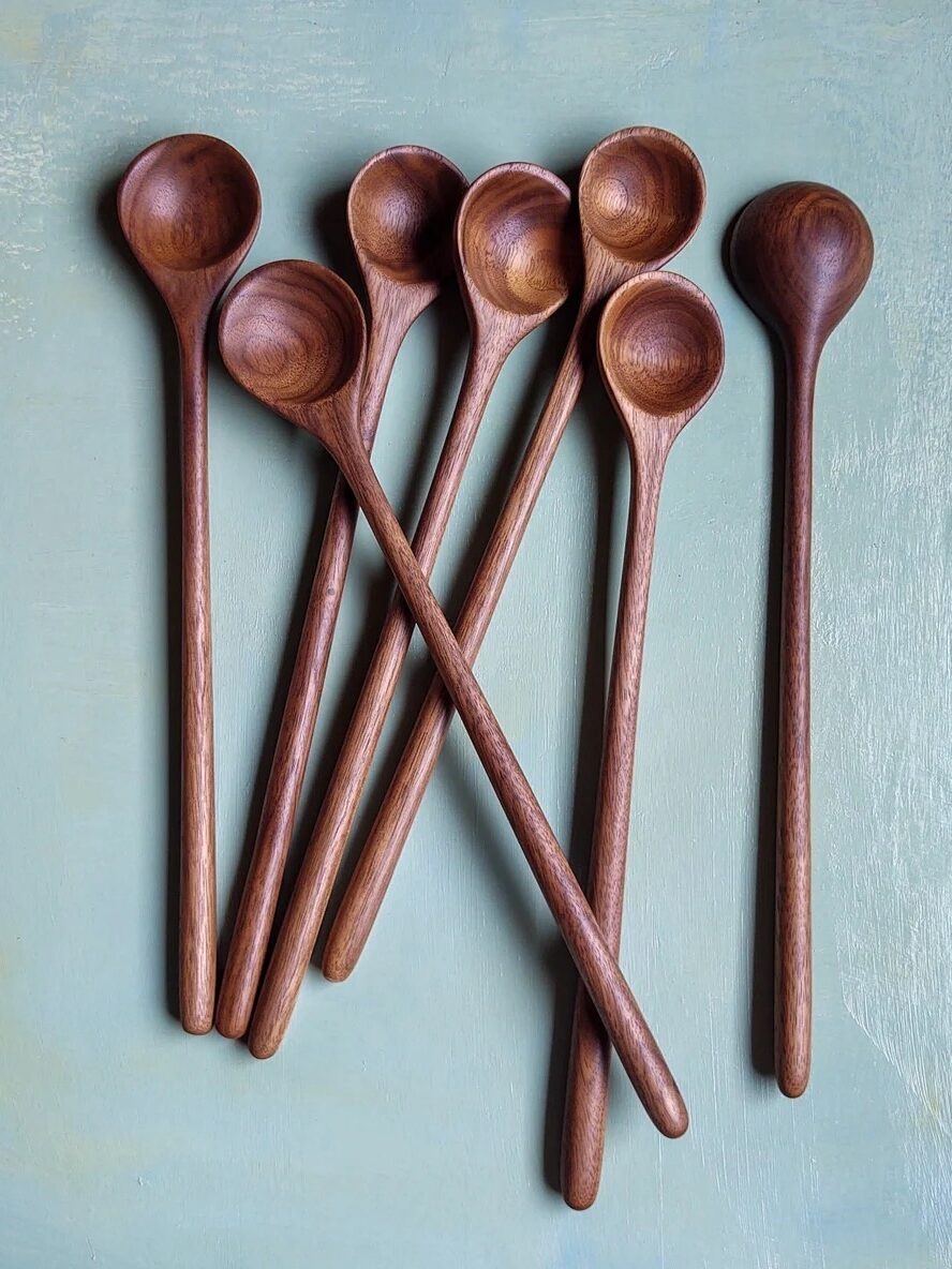 Seven wooden spoons with round bowls are arranged in a fan shape on a light blue surface.