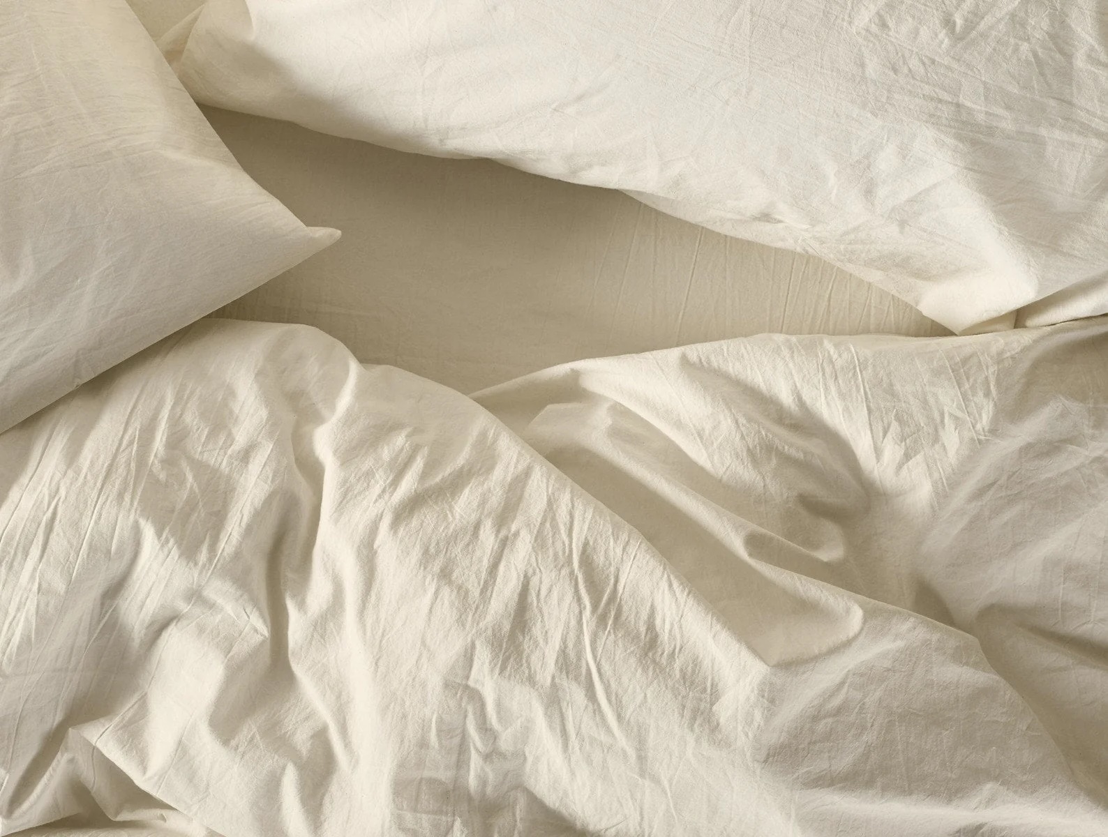 A rumpled bed with off-white sheets, a pillow, and a comforter, viewed from above.
