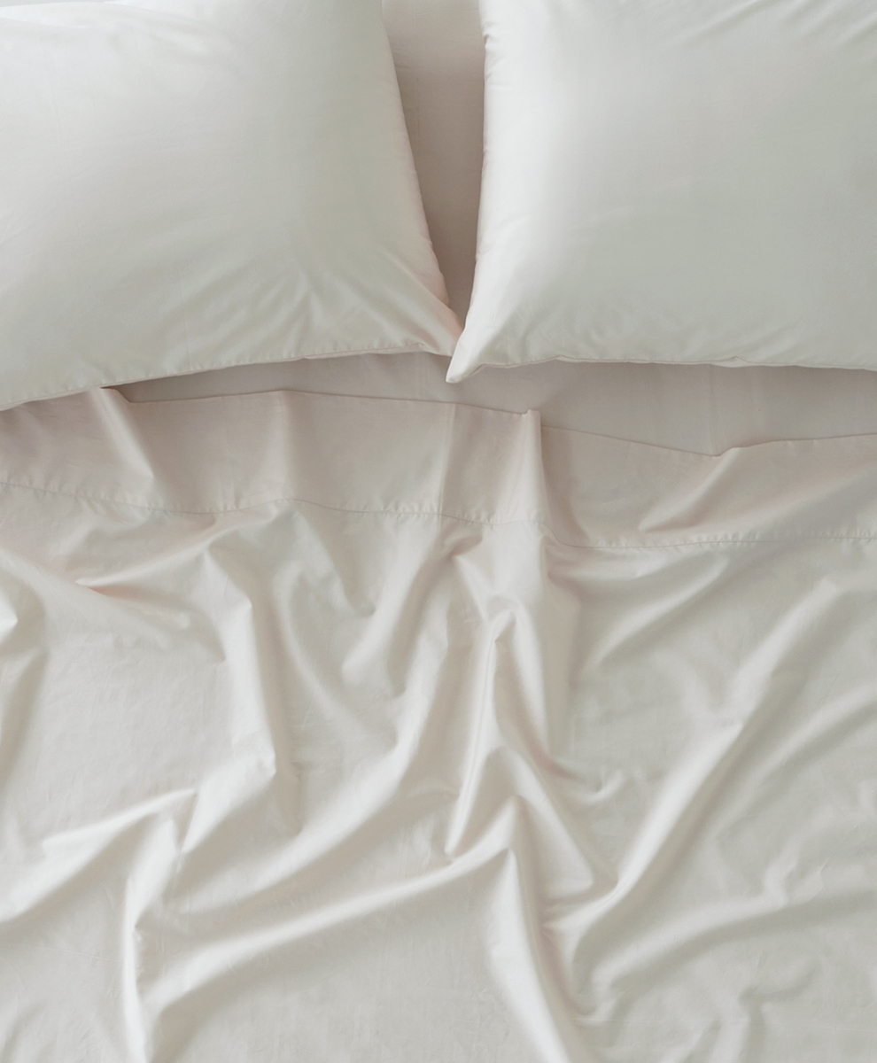Two white pillows and a white sheet with visible wrinkles and folds on a bed, viewed from above.