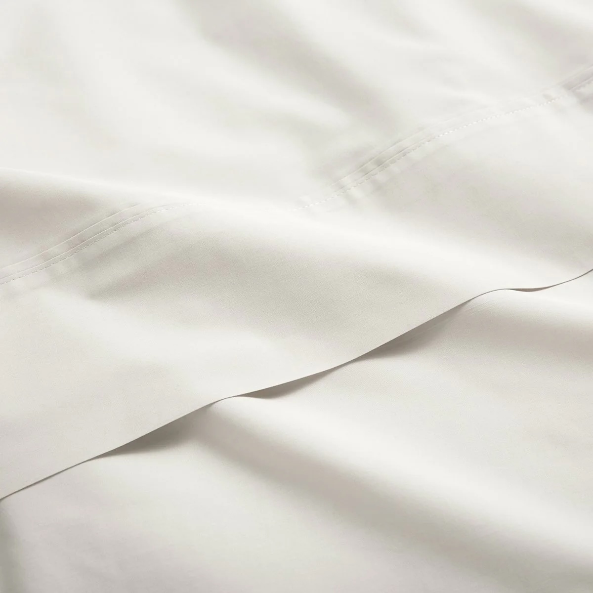 Close-up of smooth, light-colored fabric with visible stitching and a folded edge.