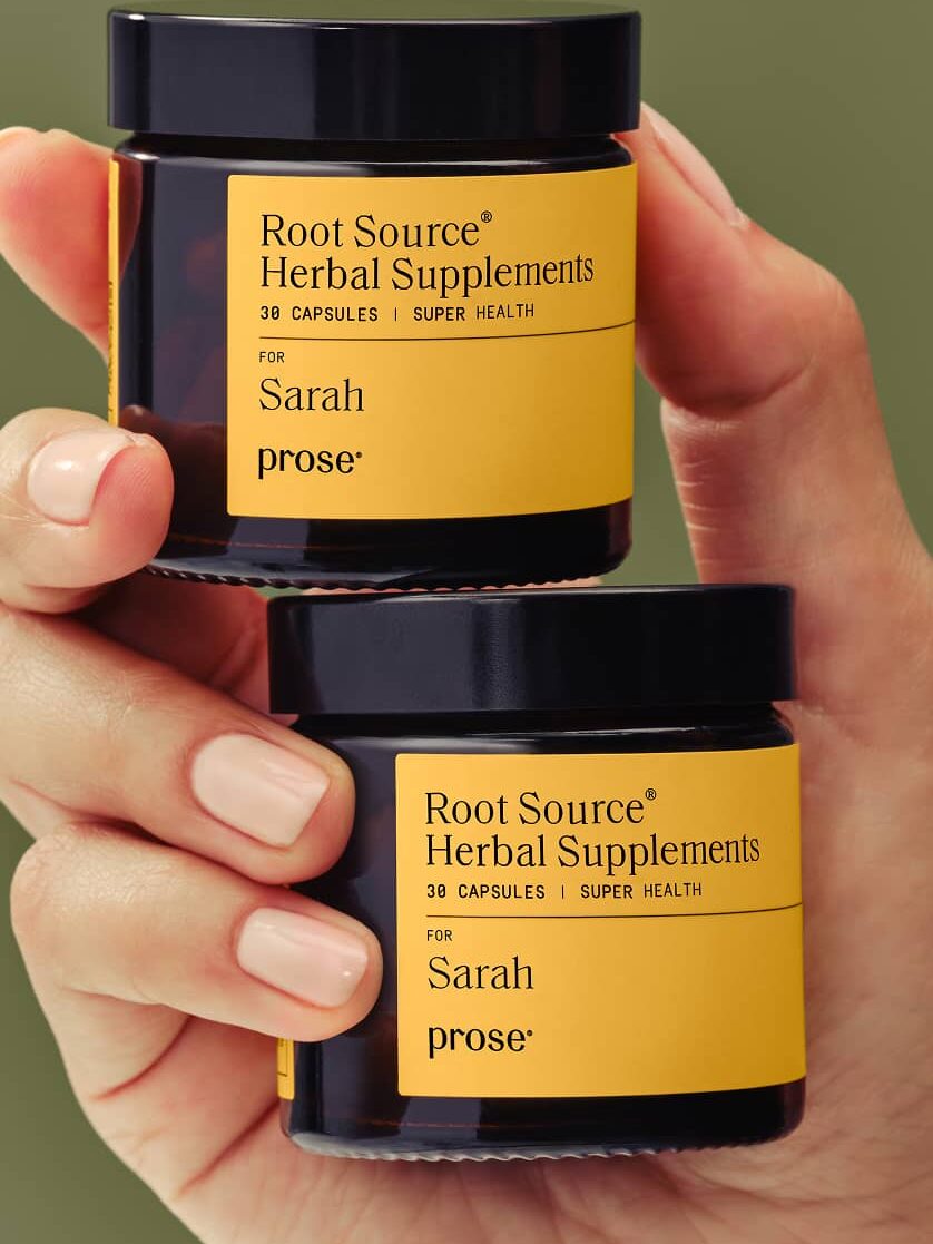 A hand holds two jars labeled "Root Source Herbal Supplements for Sarah" from the brand Prose, each containing 30 capsules.