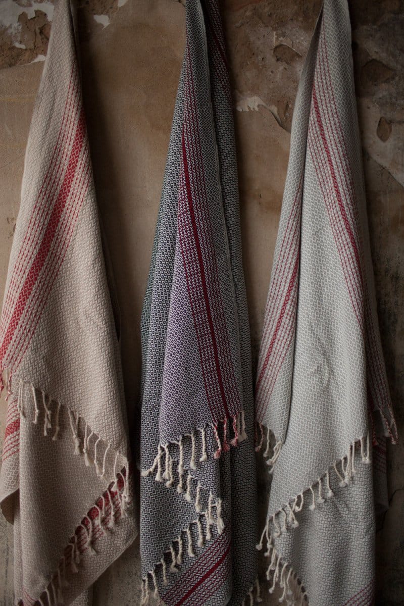 Three woven towels with red stripes and fringed edges hang on a textured, peeling wall.
