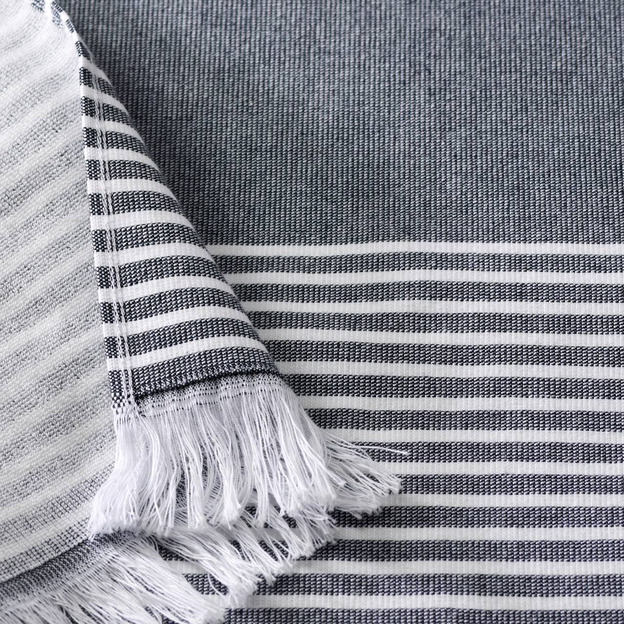 A close-up of a woven fabric with horizontal black and white stripes and fringed edges on one side.