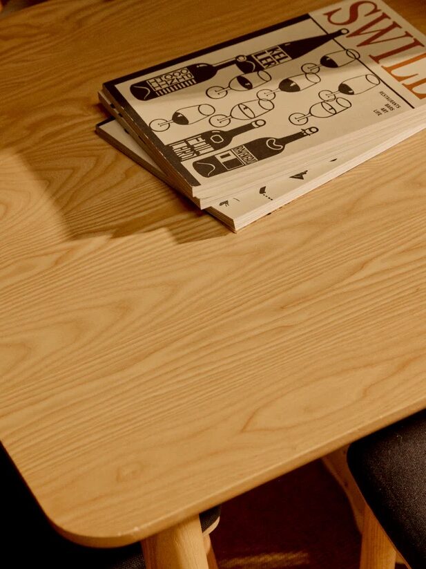 A magazine with a cover titled "SWILL" and monochrome graphics rests on a wooden table next to a dark upholstered chair.