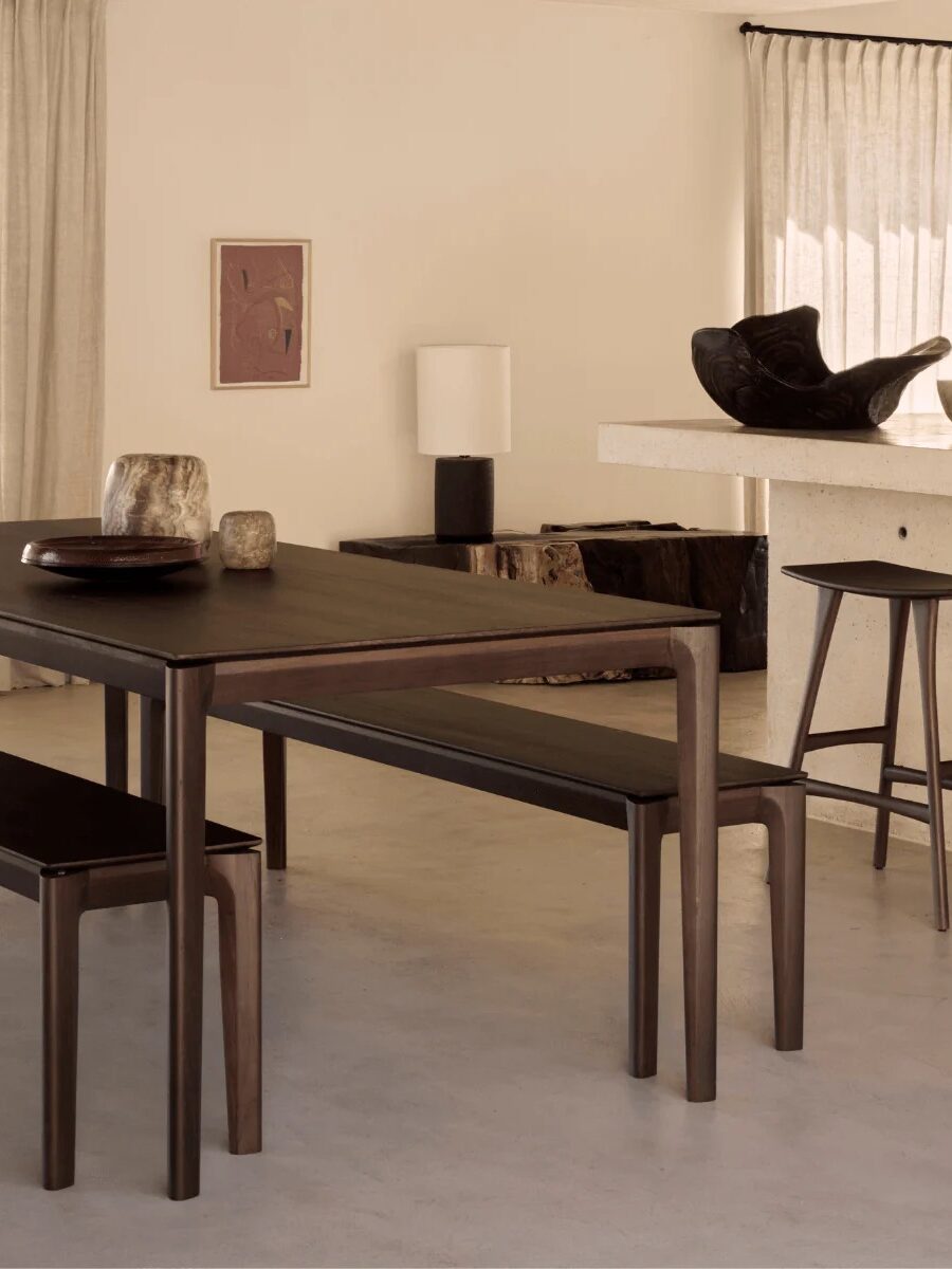A minimalist dining area features a dark wooden table with matching benches, light walls, bar stools, and simple decor in neutral tones.