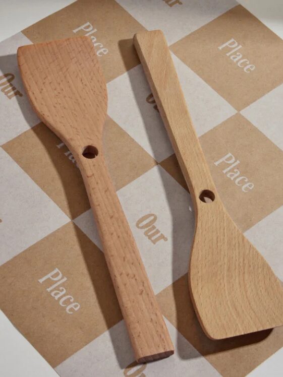 Two wooden kitchen utensils with holes in the handles are placed on a brown and white checkered paper labeled "Our Place.