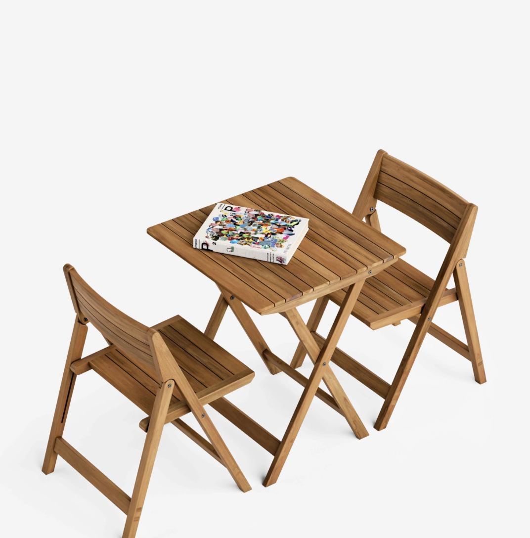 Two wooden folding chairs and a matching square table, with a magazine placed on the tabletop, all set against a white background.