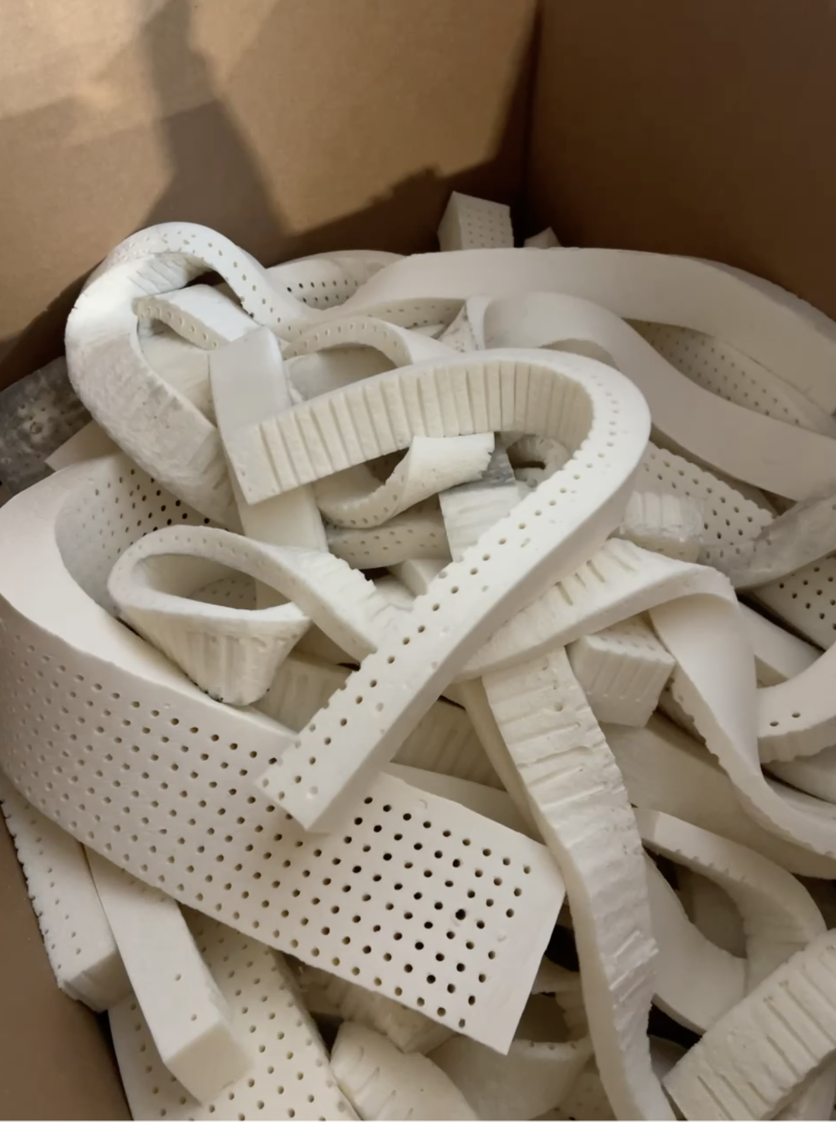 A cardboard box containing assorted white rubber or foam strips, some with perforations and textured surfaces.