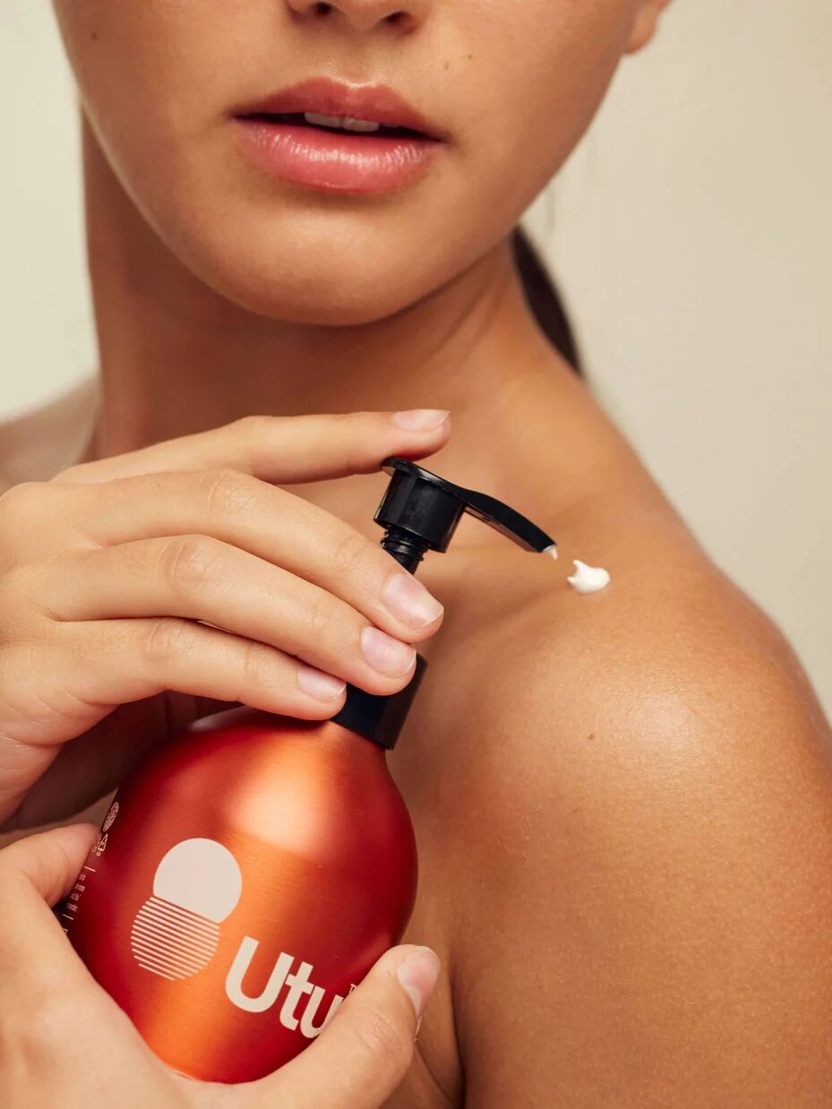 A person applies lotion to their shoulder from an orange bottle labeled "Utu.