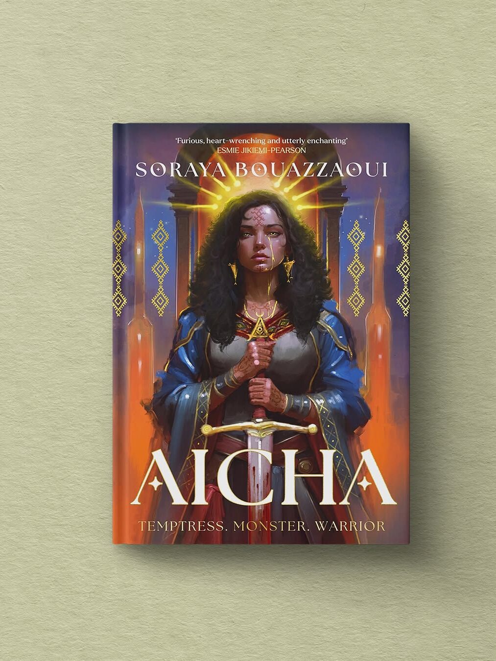 A book titled "Aïcha" by Soraya Bouazzaoui features an illustrated woman in ornate clothing holding a sword, with geometric patterns in the background. Subtext reads: "Temptress. Monster. Warrior.