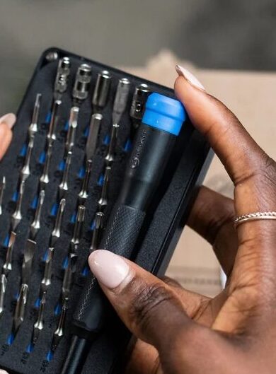 A person holds a compact toolkit with various precision screwdriver bits and a blue-handled tool, suitable for electronics repair.