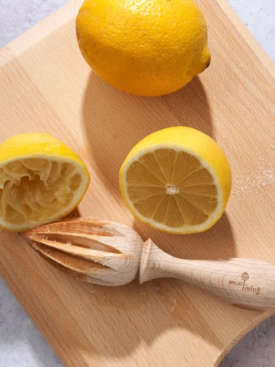 A wooden citrus reamer and a halved lemon, one half juiced, rest on a wooden cutting board with a whole lemon nearby.