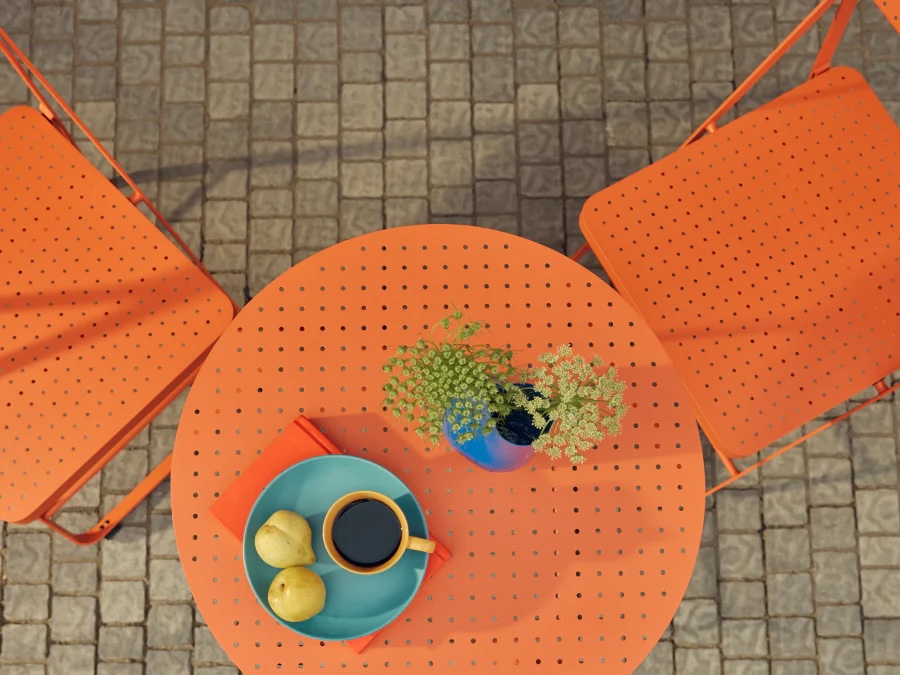 Top view of an orange metal table with two matching chairs, holding coffee, two pears on a plate, a napkin, and a small vase with assorted flowers.