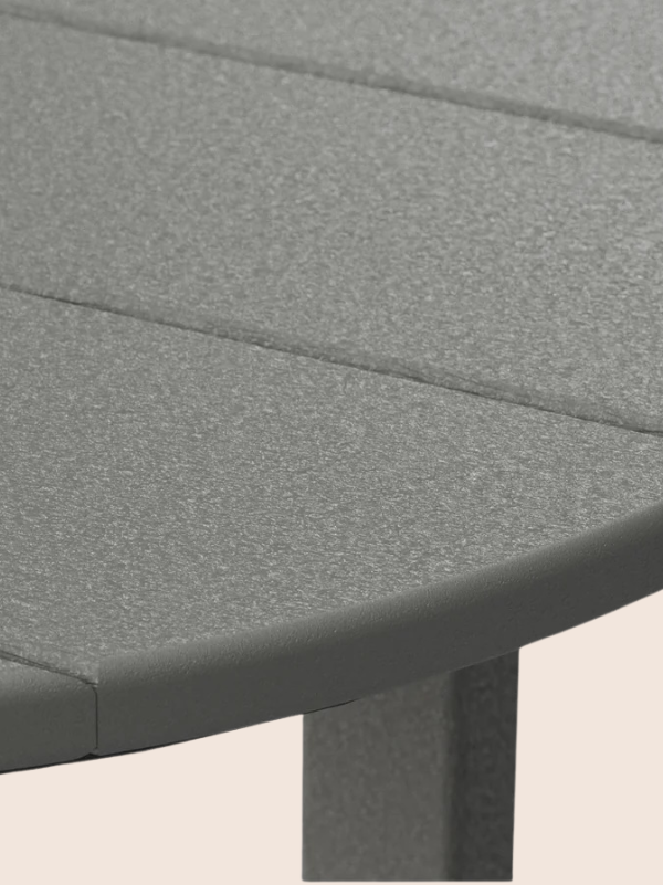 Close-up view of a round, gray, slatted table with a textured surface and vertical legs, shown against a plain light background.