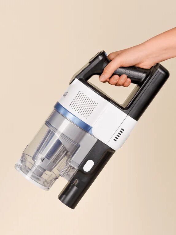 A hand holds a black and white cordless handheld vacuum cleaner against a plain beige background.